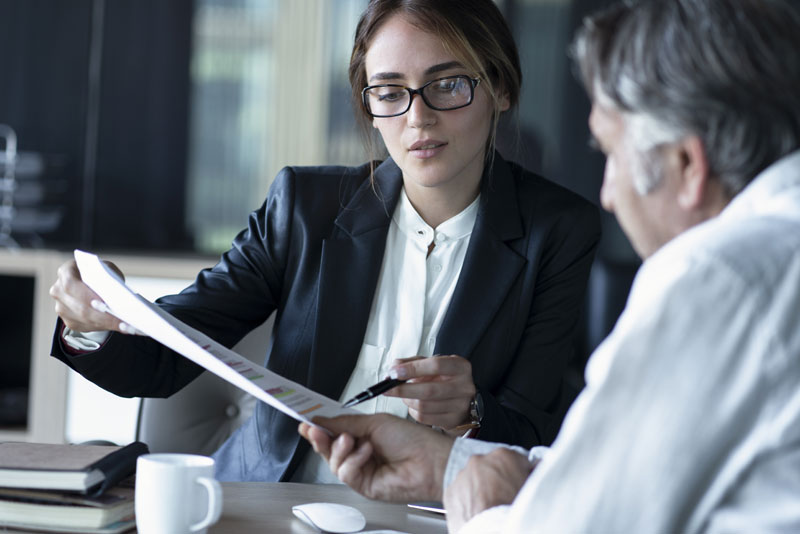 Bankangestellte berät einen Kunden und zeigt ihm die Unterlagen.