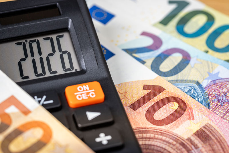 Euroscheine auf einem Tisch und ein Taschenrechner darauf mit Datum 2026.