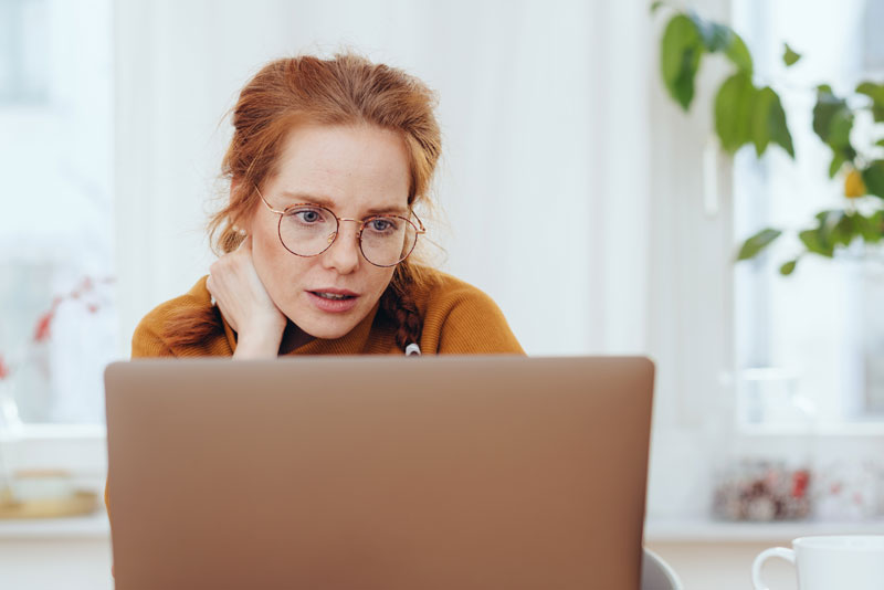 Frau mit Brille schaut nachdenklich auf das Display ihres Notebooks und denkt über einen Kredit trotz schwacher Bonität nach.