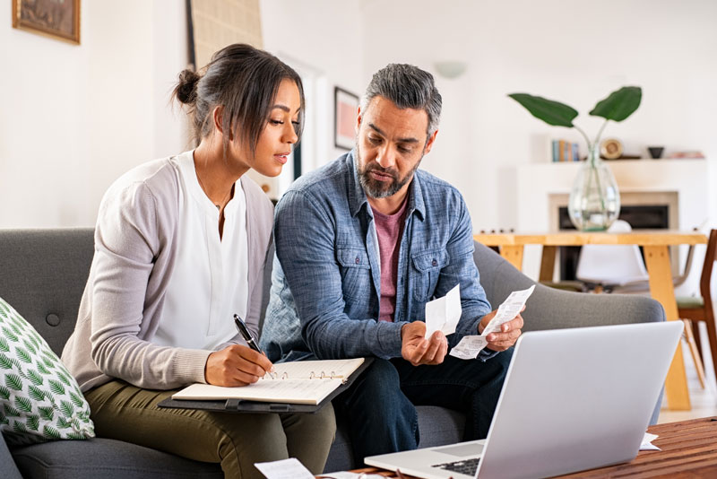 Paar plant Finanzen mit Laptop und Unterlagen am Tisch.