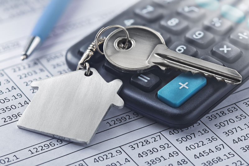 Schlüssel mit Hausanhänger auf einem Taschenrechner und Finanzunterlagen als Symbol für die Planung einer Anschlussfinanzierung und die Berechnung von Immobilienkrediten.